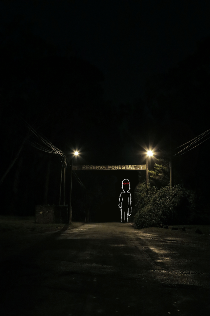 The same darkened image of the sign reading Reserva Forestal, but this time with a white figure with red eyes drawn standing under the sign.